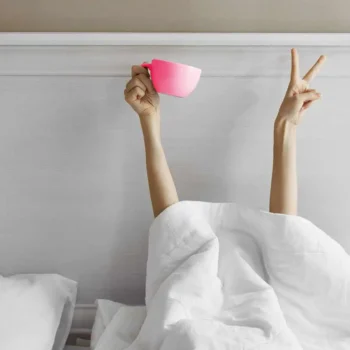person under the bed covers with coffee cup at bed and breakfast