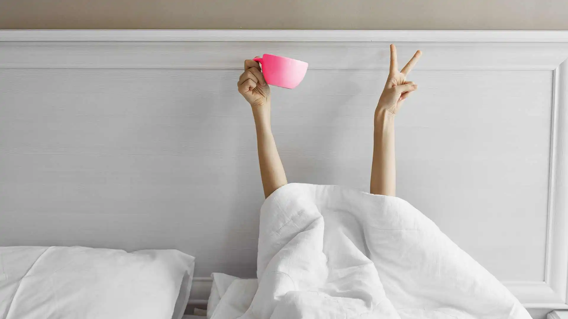 person under the bed covers with coffee cup at bed and breakfast