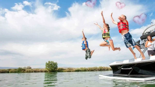 three kids jumping off back of boat into water