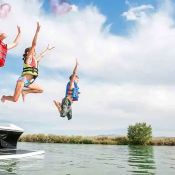 Three kids jumping off back of boat into water.