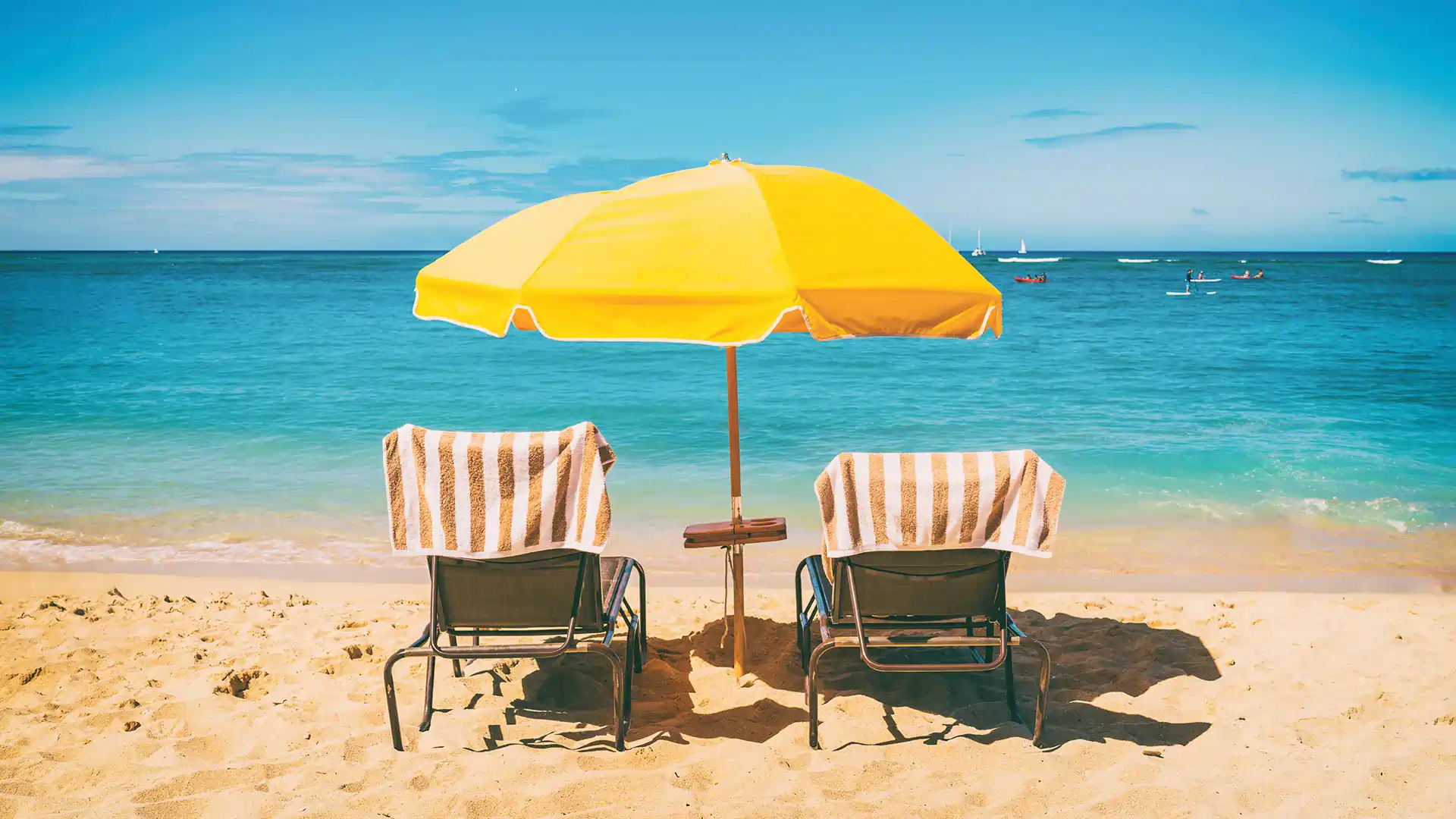 two beach chairs with towels under a yellow umbrella on a beach in a sunny vacation destination