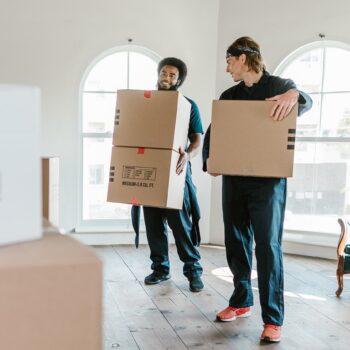 Movers carrying boxes in front of stacked boxes.
