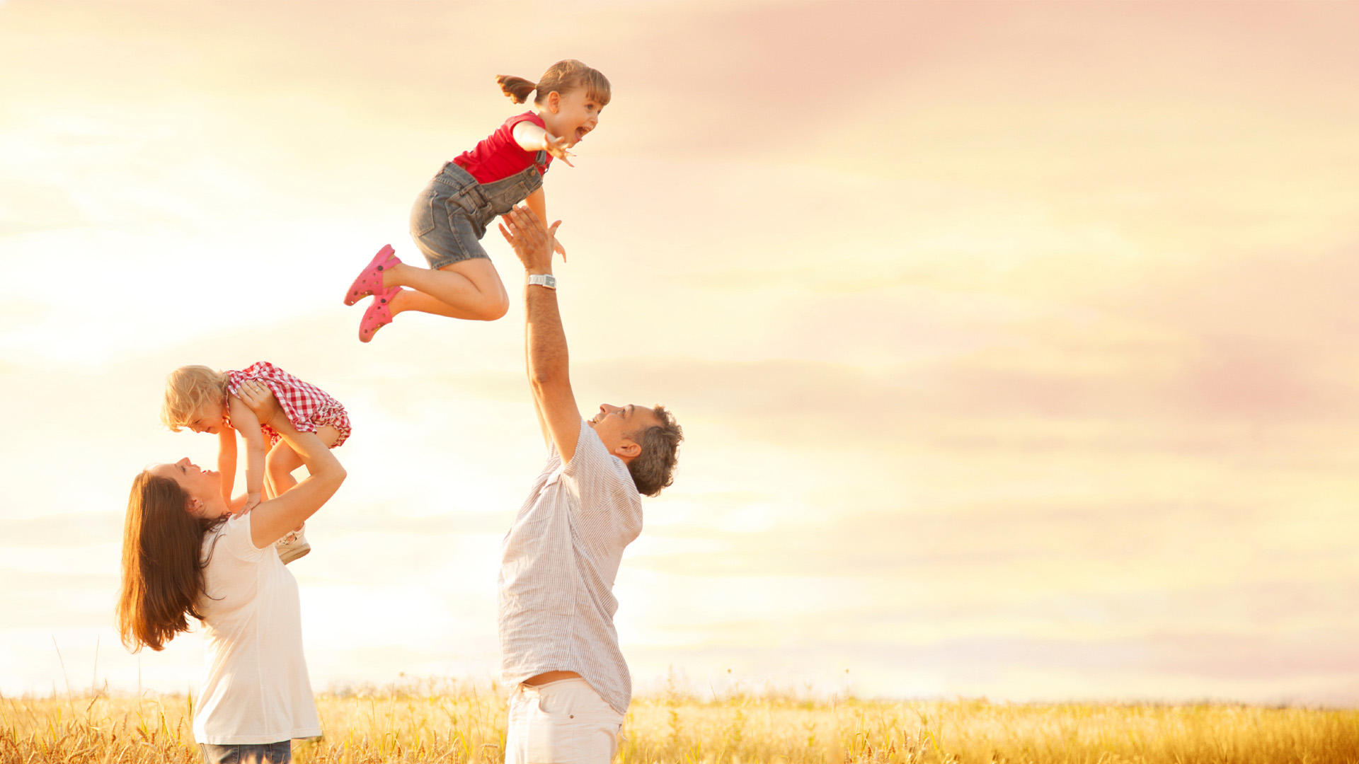 Parents tossing their children into the air, laughing, in a wheat field