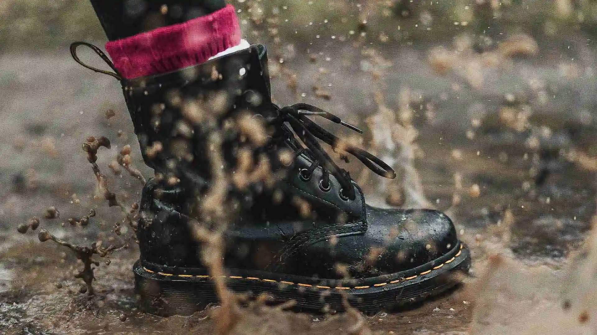 Black boot stepping in muddy puddle and splashing
