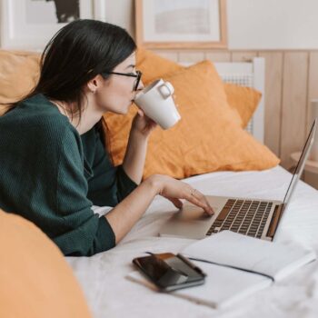 Woman on bed on laptop and drinking coffee