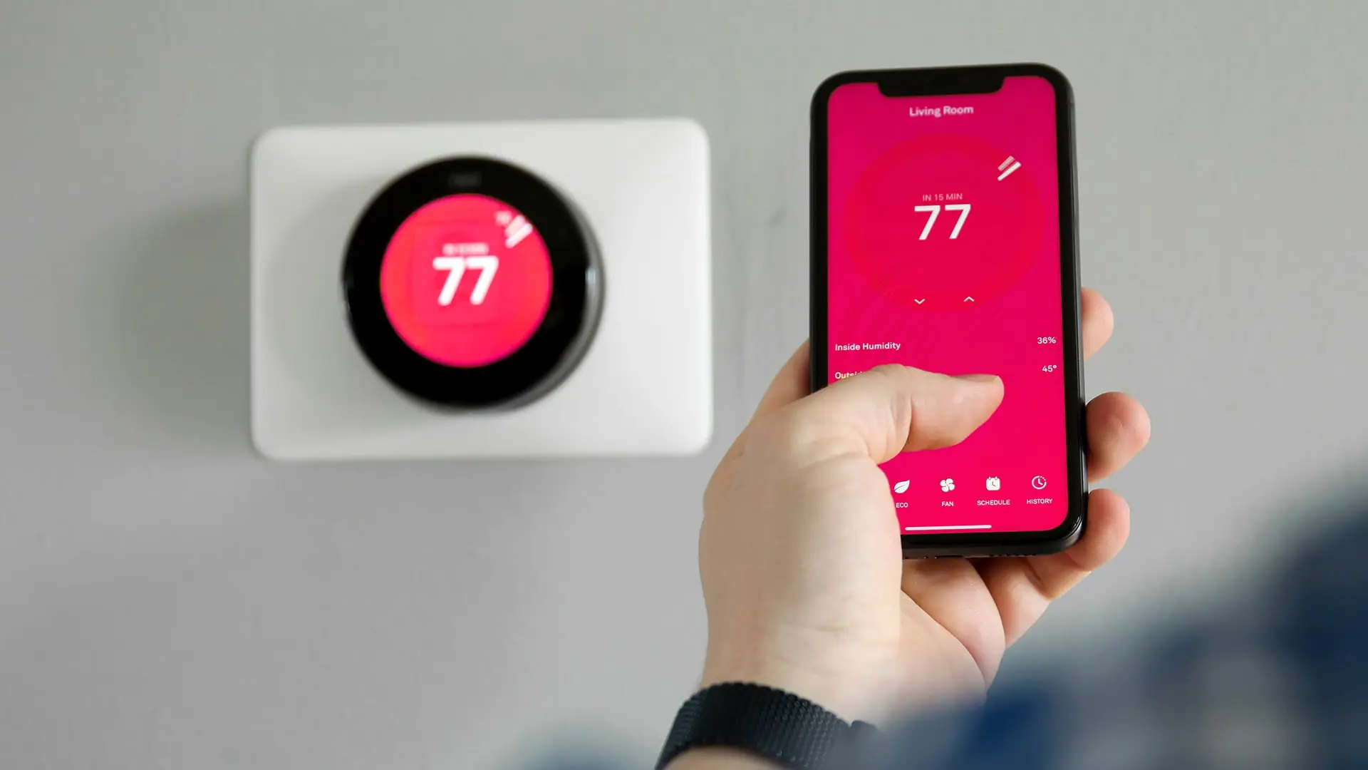 nest thermometer on wall being monitored by cell phone user on the app