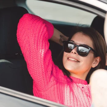woman wearing sunglasses smiling while sitting in passenger seat of car with feet out the window