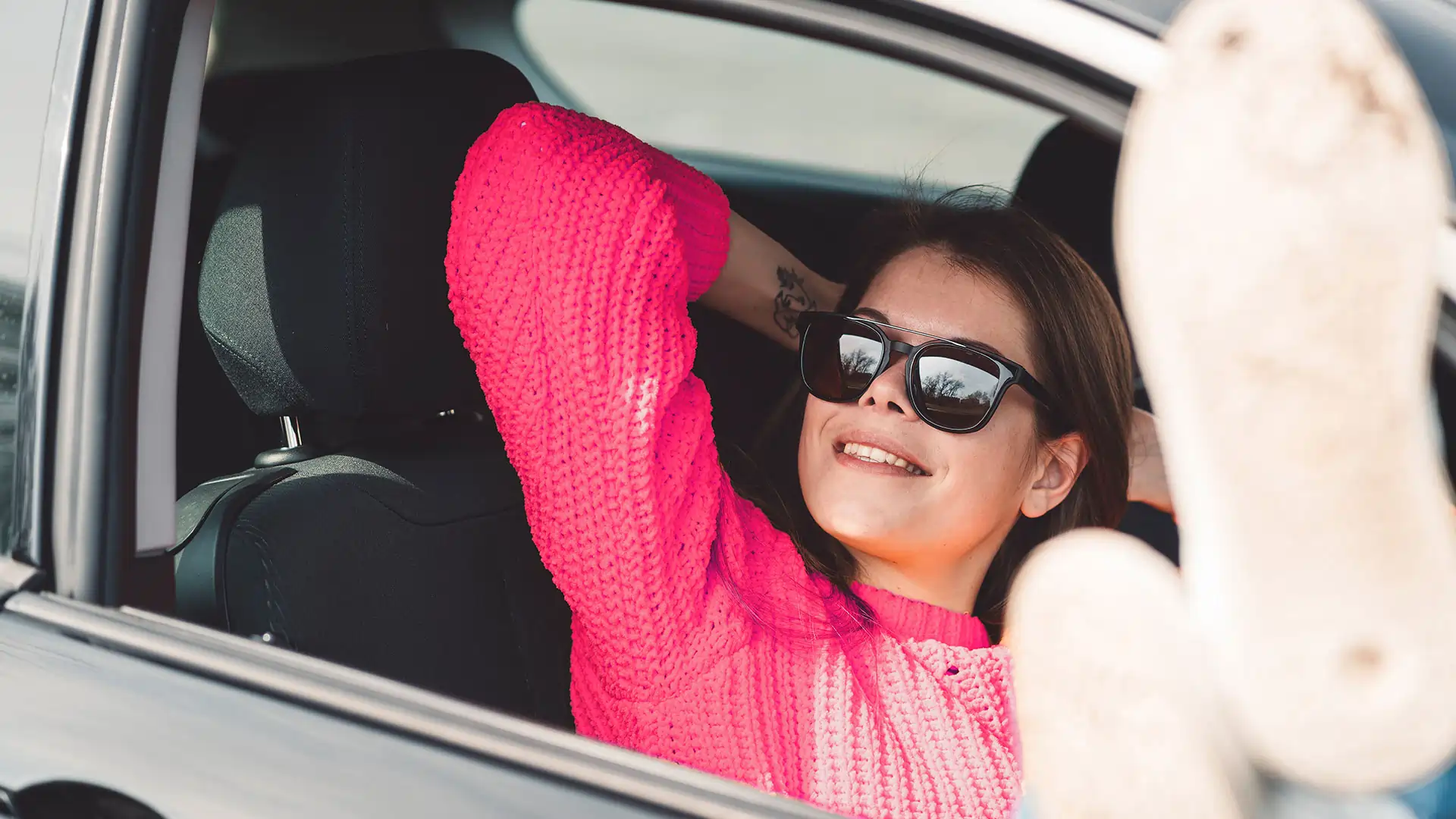 woman wearing sunglasses smiling while sitting in passenger seat of car with feet out the window
