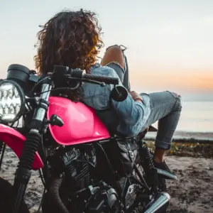 Woman laying on motorcycle on beach.