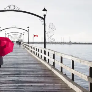 woman walking on pier holding umbrella over her head