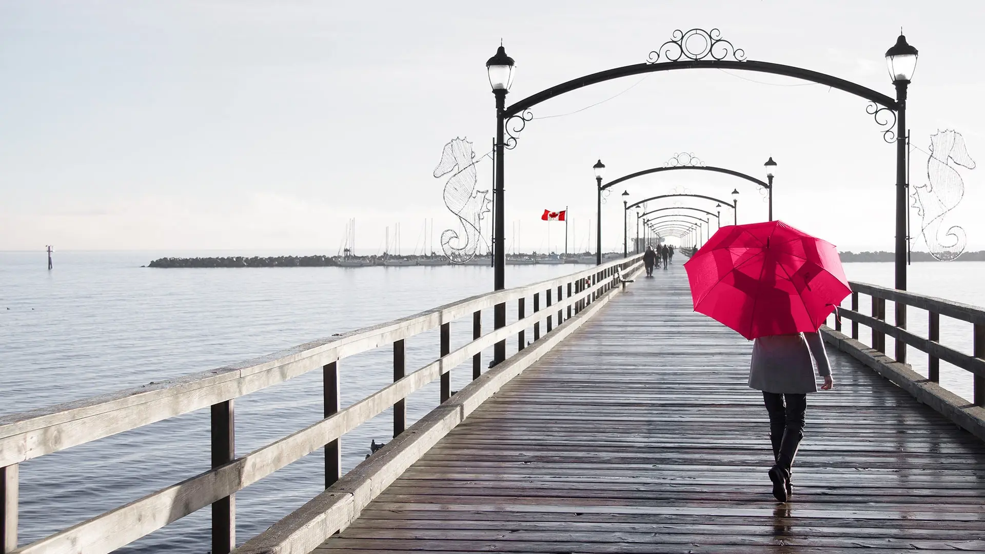 woman walking on pier holding umbrella over her head