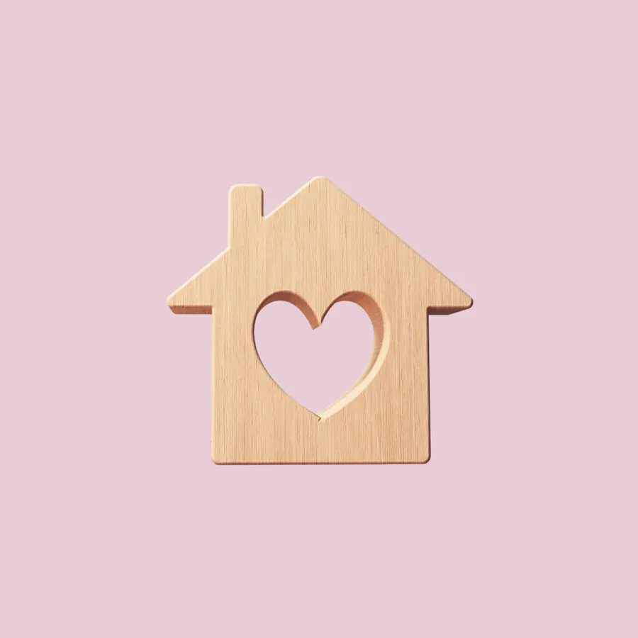 Image of a wooden house block with a heart cut out in the center on a light pink background.