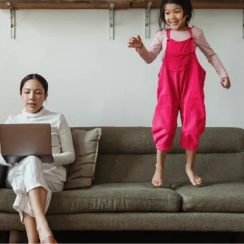 woman working on couch with kid jumping