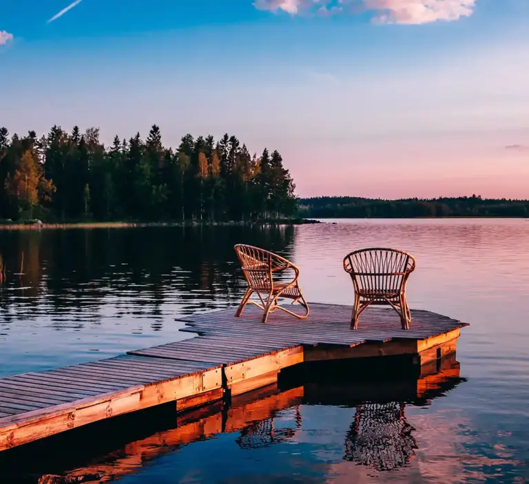 Two chair at the end of a dock on a lake at sunset.