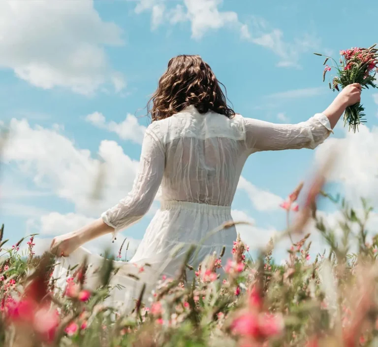 woman in white dress walking through field of wildflowers