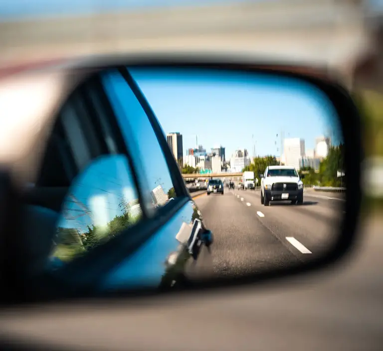 Reflection view from sideview mirror of vehicle showing vehicles driving on highway.