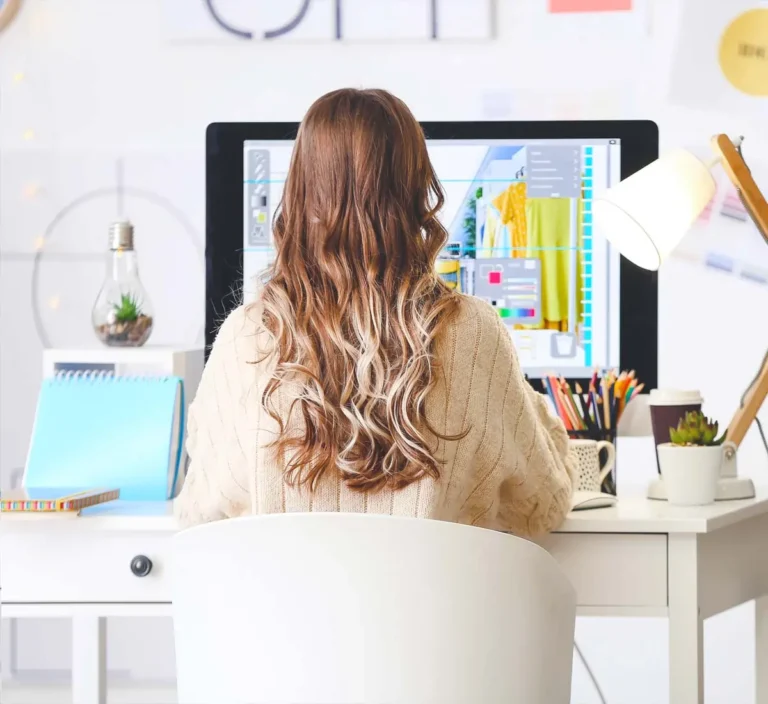 female with long blonde hair sitting at a computer desk working as a freelancer