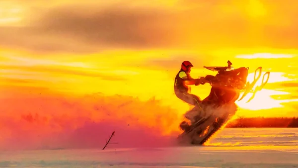 person doing a trick on a snowmobile at sunset