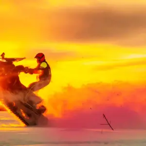 Person doing a trick on a snowmobile at sunset.