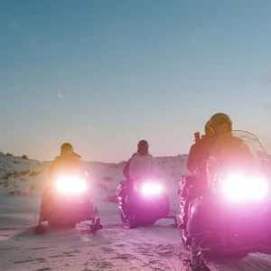 Three snowmobiles driving with their lights on at nighttime.