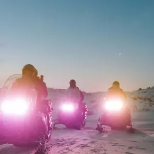 Three snowmobiles driving with their lights on at nighttime.