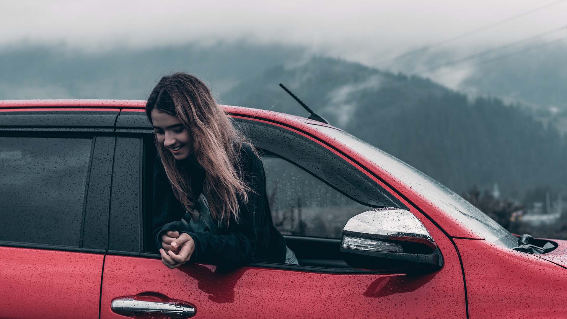 young woman with long hair hanging out of red car window