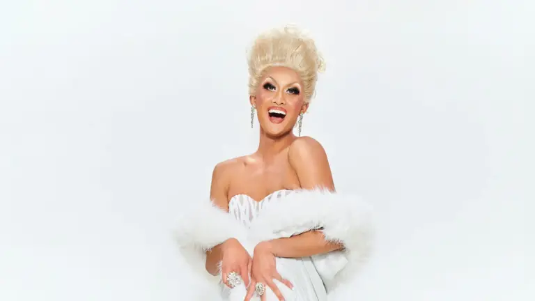 Kyne smiling in a white sequin dress and white boa.