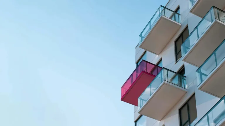 High-rise apartment building with glass balconies against a clear blue sky.