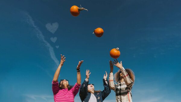 Three people throwing pumpkins in the air.