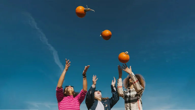 Three people throwing pumpkins in the air.