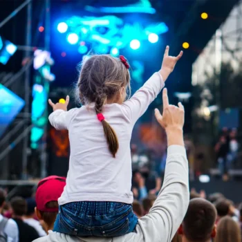 Child on the shoulders of their parent giving rocking out to a concert.