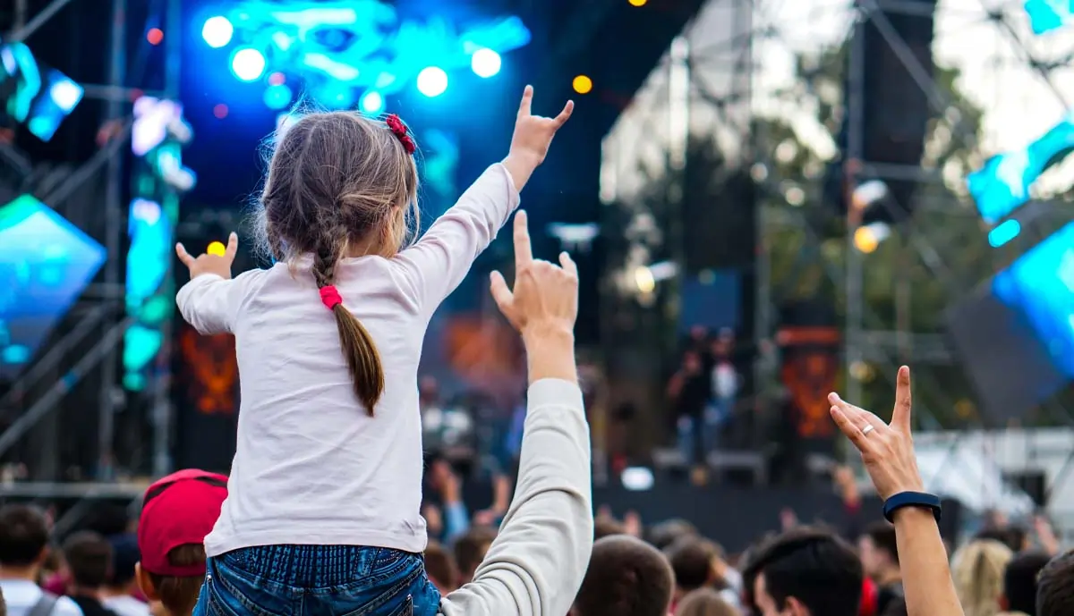 Child on the shoulders of their parent giving rocking out to a concert.