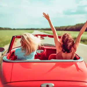 Two females driving in a convertible car through the country.